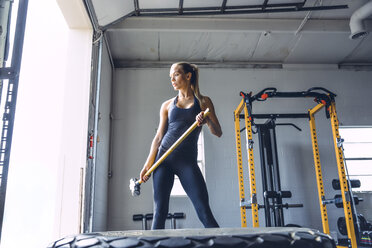 Nachdenkliche Frau, die einen Vorschlaghammer hält, während sie im Fitnessstudio trainiert - CAVF29131