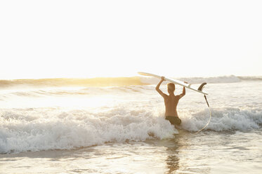 Jugendlicher mit Surfbrett beim Waten im Meer in Costa Rica - FOLF01359