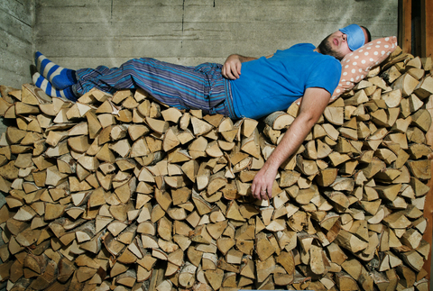 Mann schläft auf einem Stapel Brennholz, lizenzfreies Stockfoto