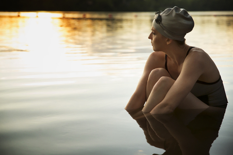 Nachdenkliche Schwimmerin am See sitzend, lizenzfreies Stockfoto