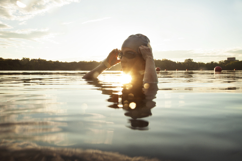 Schwimmerin mit Schwimmbrille im See bei Sonnenuntergang, lizenzfreies Stockfoto