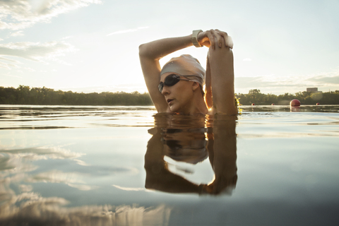 Schwimmerin streckt Arme im See gegen den Himmel, lizenzfreies Stockfoto