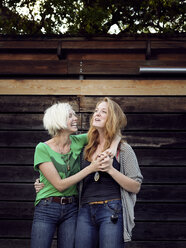 Happy sisters standing against wooden wall - CAVF29157