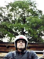 Low angle view of male biker wearing helmet against tree - CAVF29161