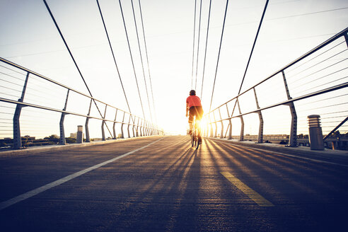 Rückansicht eines Mannes, der mit dem Fahrrad auf einer Brücke gegen einen klaren Himmel an einem sonnigen Tag fährt - CAVF29167