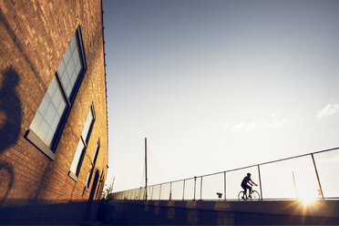 Radfahrer auf dem Fahrrad vor einem Gebäude bei klarem Himmel - CAVF29169