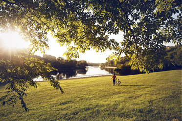 Mann mit Fahrrad auf grasbewachsener Wiese am See im Park an einem sonnigen Tag - CAVF29170