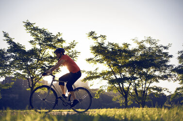 Seitenansicht eines Mannes, der mit dem Fahrrad an Bäumen vorbeifährt, bei klarem Himmel im Park - CAVF29173