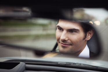 Close-up of handsome man in car reflecting on rear-view mirror - CAVF29174