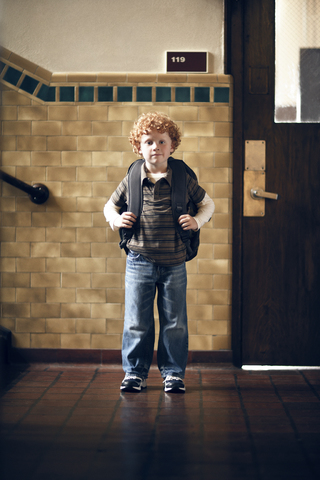 Porträt eines Jungen, der einen Rucksack trägt und vor einem Klassenzimmer steht, lizenzfreies Stockfoto