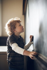 Side view of schoolboy drawing on blackboard - CAVF29196