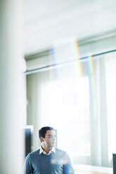 Thoughtful businessman standing in office seen through window - CAVF29208