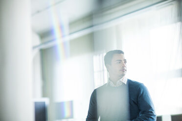 Thoughtful man standing in office seen through glass window - CAVF29209