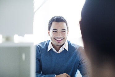 Confident smiling businessman sitting at office desk against window - CAVF29222