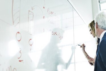 Älterer Mann betrachtet Geschäftsfrau, die im Büro auf ein Whiteboard schreibt - CAVF29240