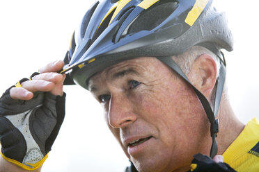 Nahaufnahme eines älteren Radfahrers, der seinen Helm gegen den klaren Himmel berührt - CAVF29251