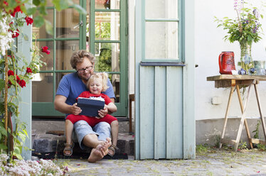 Daughter with father sitting on stone step and holding tablet pc - FOLF01486