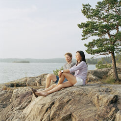 Paar im mittleren Erwachsenenalter sitzt auf Felsen und schaut aufs Meer - FOLF01595