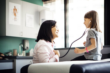 Side view of girl listening to heartbeat of female doctor through stethoscope in clinic - CAVF29295