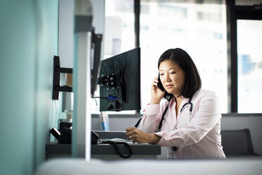 Weiblicher Arzt mit Smartphone Computer Schreibtisch in der Klinik - CAVF29306