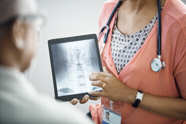 Midsection of female doctor showing x-ray on tablet computer to patient - CAVF29308