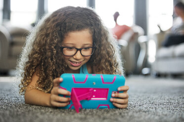 Mädchen spielt ein Handheld-Videospiel, während sie zu Hause auf dem Teppich liegt - CAVF29327
