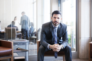 Porträt eines Geschäftsmannes, der mit gefalteten Händen in einem Büro sitzt - CAVF29348