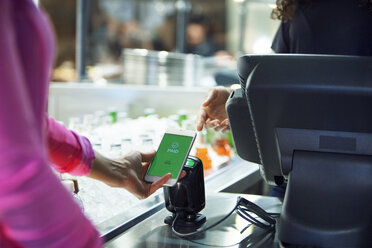 Abgeschnittenes Bild eines Kunden, der seine Rechnung mit seinem Smartphone in einem Restaurant bezahlt - CAVF29353