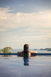 Rear view of woman in swimming pool enjoying view of Costa Rica against cloudy sky - CAVF29357