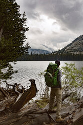 Hiker carrying backpack while standing on driftwood by river at Yosemite National Park - CAVF29362