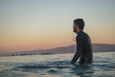 Seitenansicht eines männlichen Surfers im Meer gegen den klaren Himmel bei Sonnenuntergang, lizenzfreies Stockfoto