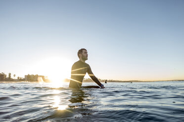 Nachdenklicher Surfer sitzt auf einem Surfbrett im Meer gegen den klaren Himmel bei Sonnenuntergang - CAVF29393