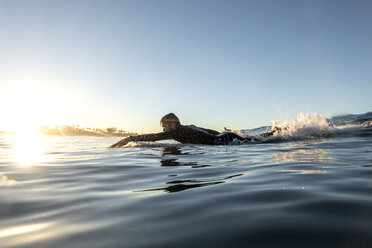 Seitenansicht eines männlichen Surfers, der bei Sonnenuntergang auf einem Surfbrett im Meer liegt - CAVF29394