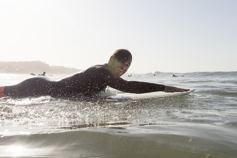 Seitenansicht Porträt der glücklichen männlichen Surfer liegen auf Surfbrett im Meer während des Sonnenuntergangs, lizenzfreies Stockfoto