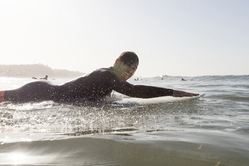 Seitenansicht Porträt der glücklichen männlichen Surfer liegen auf Surfbrett im Meer während des Sonnenuntergangs - CAVF29400