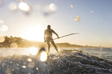 Surfer hält Stange beim Surfen im Meer bei Sonnenuntergang - CAVF29401