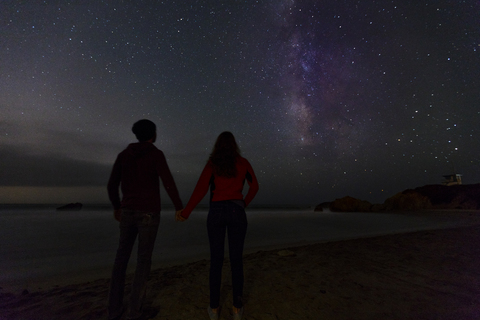 Rückansicht eines Paares, das sich an den Händen hält und den nächtlichen Sternenhimmel betrachtet, lizenzfreies Stockfoto