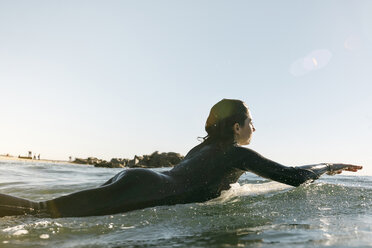 Side view of female surfer lying on surfboard in sea against clear sky - CAVF29418