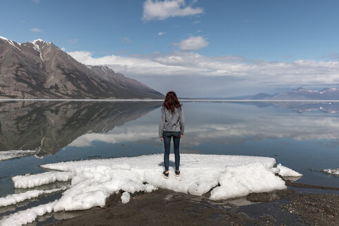 Frau steht auf Schnee am Fluss und betrachtet die Aussicht auf Berge und Himmel - CAVF29421