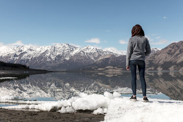 Frau in voller Länge auf Schnee am Fluss stehend, mit Blick auf Berge und Himmel - CAVF29422