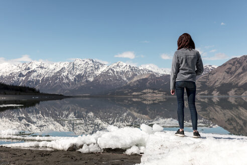 Frau in voller Länge auf Schnee am Fluss stehend, mit Blick auf Berge und Himmel - CAVF29422