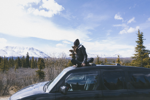 Frau betrachtet die Aussicht, während sie auf dem Autodach im Denali-Nationalpark sitzt, lizenzfreies Stockfoto