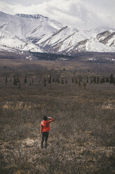 Rückansicht einer Frau, die auf einem Feld vor schneebedeckten Bergen im Denali National Park steht - CAVF29428