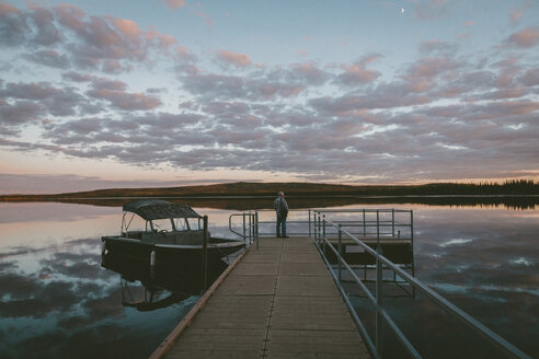Mann steht auf Pier über Fluss gegen bewölkten Himmel bei Sonnenuntergang - CAVF29431