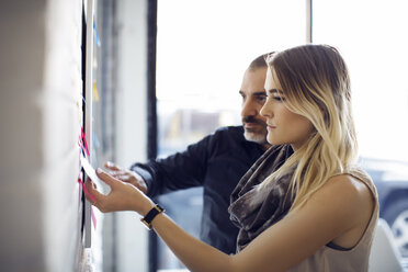 Business people sticking adhesive notes on wall at creative office - CAVF29453