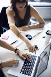 Businesswomen using laptop while discussing in creative office - CAVF29459