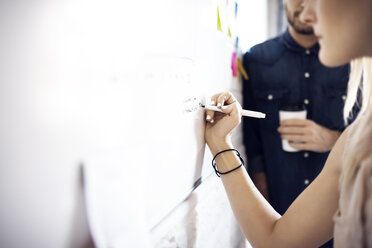 Geschäftsfrau schreibt am Whiteboard, während ein Kollege im Hintergrund steht - CAVF29471