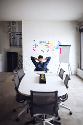 Rückansicht eines Geschäftsmannes mit Blick auf Haftnotizen, der auf einem Stuhl in einem kreativen Büro sitzt - CAVF29492