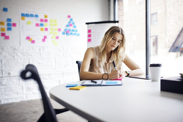 Businesswoman writing on adhesive note at table in office - CAVF29503