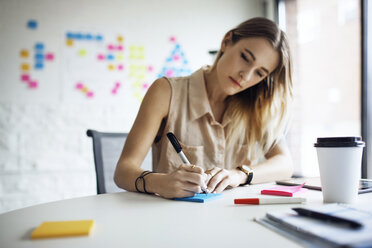 Serious businesswoman writing on adhesive notes at table in office - CAVF29507